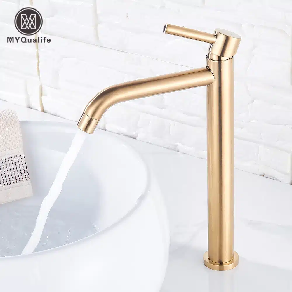 Elegantselt disainitud kuldne kraan vannituppa, millel on sirge toru ja peenike käepide. Kraanist voolab vesi valgesse kraanikaussi, taustal valged keraamilised plaadid.