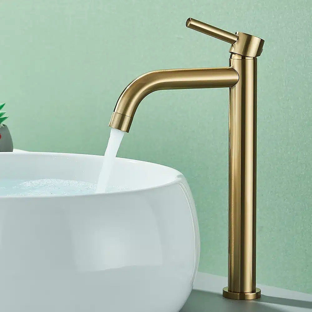 Kuldne kraan vannituppa, elegantse disainiga, voolab vett valgesse ovaalsesse kraanikaussi rohelisel taustal.