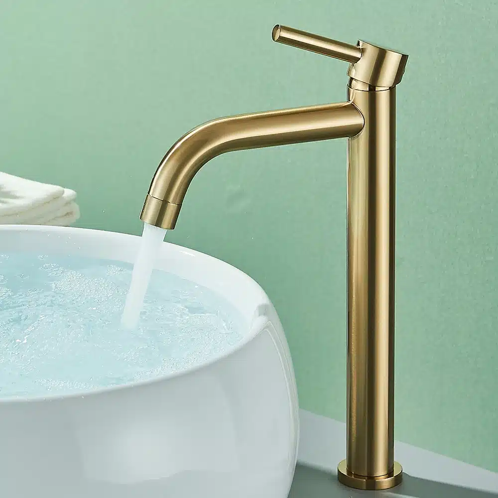 Elegantne kuldne kraan vannituppa, mille voolujooneline disain täiustab kaasaegset valget valamukaussi. Taust on rahustava pastellrohelise seinaga, rõhutades kraani luksuslikku välimust.