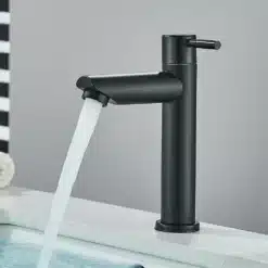 Must, ühe käepidemega Vannitoa külm veepump kraan, millest voolab vesi valge portselanist kraanikaussi halli seina taustal.