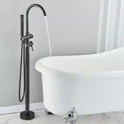 Põrandale paigaldatav vannisegisti käsidušiga, musta viimistlusega, modernse välimusega, elegantselt paigutatud valge vanni kõrvale heledal taustal.