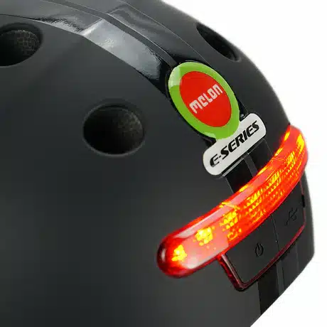 Kiiver MELON E-Series, Black Ice (XL) musta värvi läikiva viimistlusega, millel on punane LED-valgus, mustad ventilatsiooniavad ja stiilne disain linna jaoks.