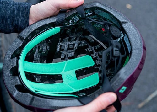 Lähivõte jalgrattakiivriga LAZER Tempo KinetiCore CECPSC, must, mille sees on rohelised vahupolstrid ja turvarihmad. Kiivrit hoitakse käes, mis toetab selle vastupidavat konstruktsiooni.