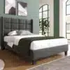 Elegantne üheinimesevoodi pehme peatsiga, viimistletud halli linakangaga mõõtmetega 90x200 cm. Taustal on rohelised seinad ja suured aknad, luues hubase magamistoa meeleolu.