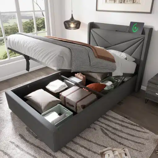 Kaasaegne üheinimese voodi koos avatud panipaigaga, millel on hall pehme kangas, mugav madrats ja sisseehitatud USB Type-C laadija. Valgustatud magamistuba linnamulje aknaga taustal.