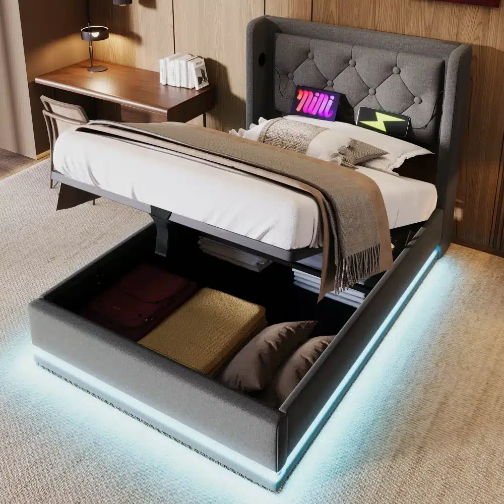 Hall Voodi pesukastiga, USB ja LED-valgustusega 90×200, avatud pesukastiga, voodil valged linad ning tumepruun tekk. Taustal on puidust kirjutuslaud ja valgusti.