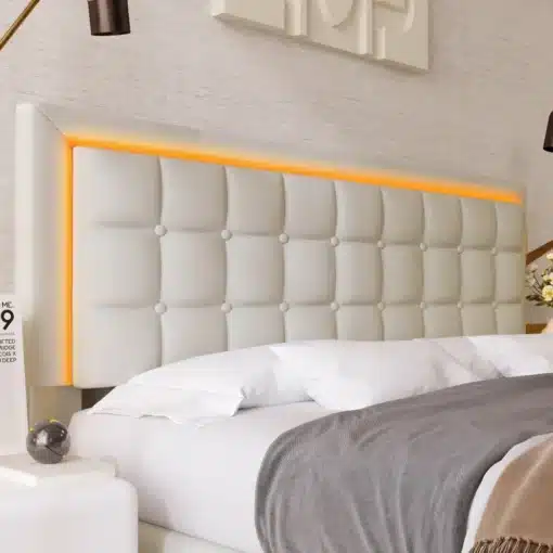 Pesukastiga voodi, LED-valgustusega 140x200, heledast kangast voodi, millel on oranž LED-valgustusega peats. Taustal on neutraalsed seinad ning dekoratiivsed elemendid.