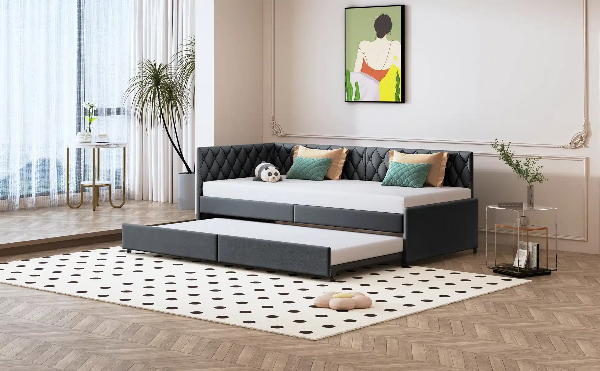 Diivanvoodi ratastel sametist, hall 90x200 cm, elegantses elutoas valgusküllase akna kõrval, millel on kerged kardinad ja põrandale ulatuv vaip. Diivanil on mitmevärvilised padjad ja kaval polsterdus, mis pakub mugavust ja funktsionaalsust.