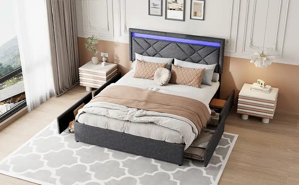 Lai tumehall voodi pesukastidega, millel on peatsis sinine LED-valgustus. Voodi on asetatud stiilsesse magamistuppa, kus on heledad seinad ja aknavaade. Mõlemal küljel asetsevad modernsed öökapid. Voodil on pehmed, neutraalsetes toonides voodipesud.