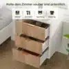 Valge ja naturaalne öökapp kolme sahtliga, mille kumerad käepidemed on messingist. Öökapp asub valgusküllases toas ja sobib hästi voodi kõrvale, rõhutades mugavust ja stiili. Sahtlid on avatud, näidates võimalust hoiustada erinevaid esemeid.