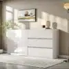 Stiilne kapp LED-valgustusega, valge läikiva viimistlusega, esitleb kahte ust ja kolme sahtlit avaras ja valgusküllases toas halli seina taustal.