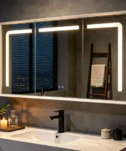 Elegantne vannitoakapp LED valgustusega, 3 uksega, valge viimistlusega, paigaldatud modernsesse tumehallides toonides vannituppa. Kapi peegeluste LED valgus loob sooja ja meeldiva valguse, rõhutades minimalistlikku disaini.