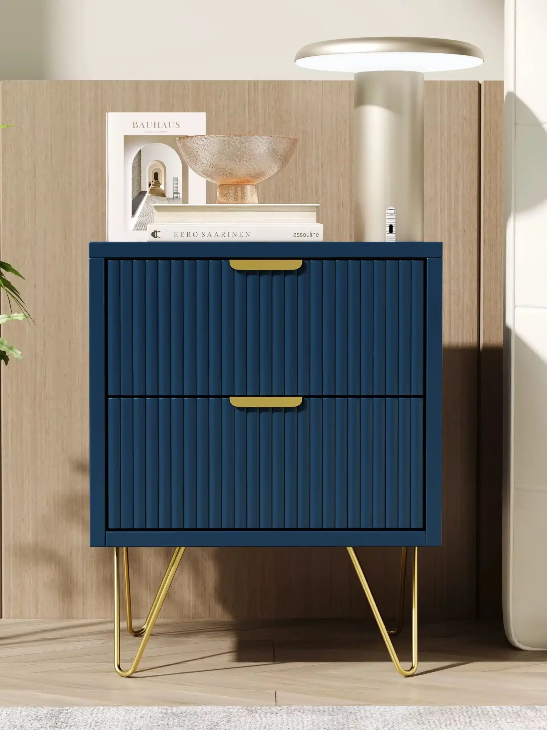 Tumesinine öökapp kahe sahtliga ja kuldsetel metalljalgadel, mille peal on valge lamp, dekoratiivobjekte ja raamatuid, asetseb puidust seina taustal.
