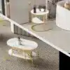 Kaunid diivanilauad marmori välimusega ja ümarate kuldsete raamidega, seismas stiilses elutoas beežil vaibal, taustal pehmed beezid ja hallid toonid.