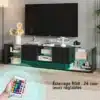 Kaasaegne must TV-alus LED-valgustusega ja kahe sahtliga, mõõtmetega 200x35x45 cm, paistab stiilselt elutoas teleriekraani all. Alusel on rohelise varjundiga LED-valgustus, raamaturiiulid ja dekoratiivsed esemed, peegeldades luksuslikku ja funktsionaalset disaini. Puidust põrandal, halli seinaga taustal ja kaugjuhtimispuldiga valgustuse reguleerimisvõimalus.