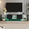 Moodne TV-alus LED-valgustusega ja kahe sahtliga, mõõtmetega 200x35x45 cm. Alus on musta värvi, klaasist külgriiulitega ja integreeritud LED-valgustusega, mis lisab elutuppa stiili ja funktsionaalsust. Alusel on paar dekoratiivset elementi, nagu lillevaas ja erinevad raamatud, mis rõhutavad selle elegantsust.