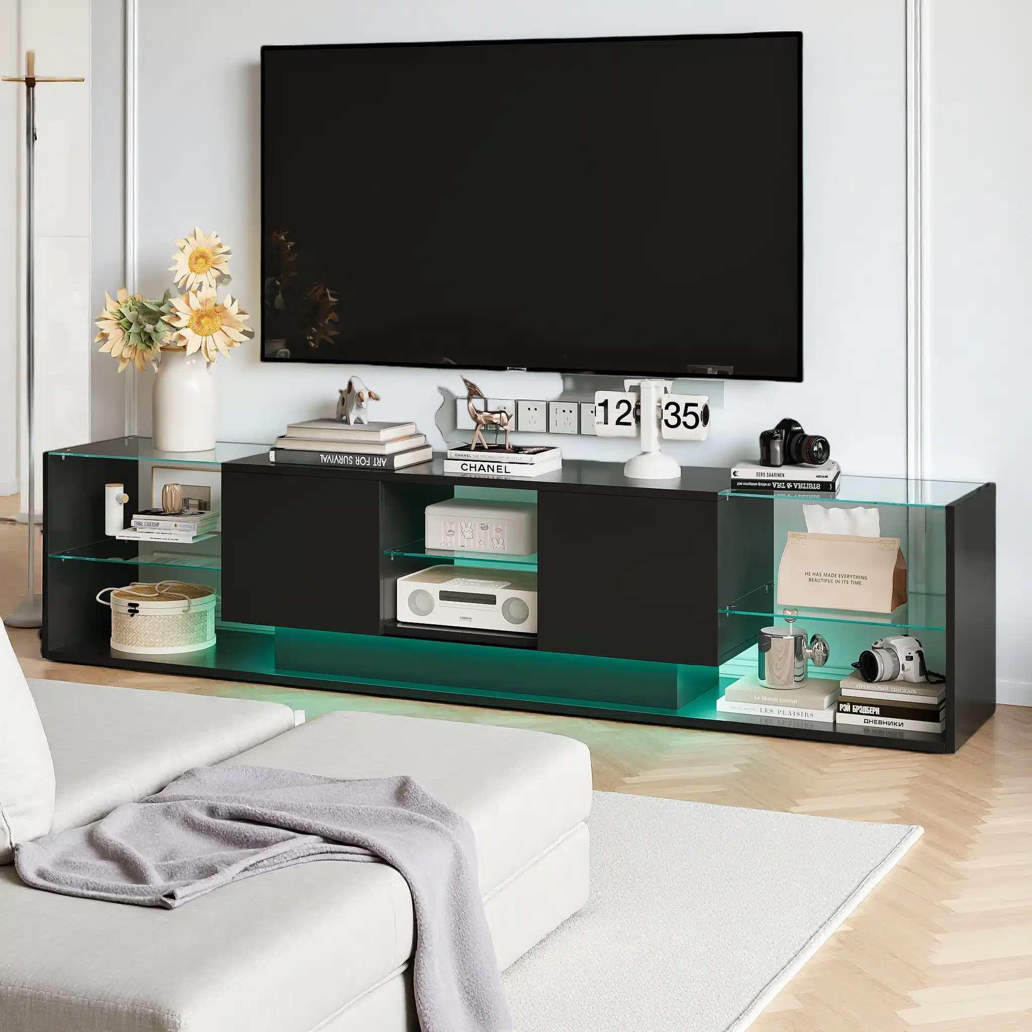 Modernne must TV-alus LED-valgustusega ja kahe sahtliga, suurusega 200x35x45 cm, paikneb avaras elutoas koos dekoreerivate elementidega nagu raamatud ja kaamera, mille taustaks on hele sein ja hele puitpõrand.
