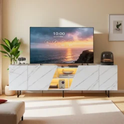 Tv-alus LED-valgustusega, valge marmoriefektiga, pikkusega 220 cm. Alusel on kaasaegne disain, marmorimustriga esipaneelid ja sisemine LED-valgustus, mis loob stiilse õhkkonna elutoas. Toode seisab valgusküllases ruumis taustal pruunid ja rohelist tooni elemendid.