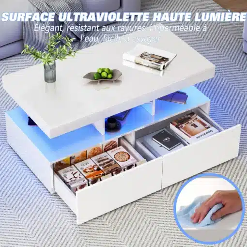 Läikiv valge diivanilaud LED valgustusega, millel on riiulid ja sahtlid. Laua peal on dekoratiivne kauss ja ajakiri ning taustal hall diivan, mis toetavad kaasaegset disaini. Sinise LED-valgustuse abil paistavad riiulid ja esemed sahtlites esile.