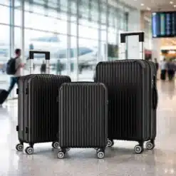 Kolm musta värvi kõvakestaga kohvrit, erineva suurusega ja varustatud TSA lukuga, asuvad lennujaama terminali heledal põrandal, taustal suur akendega sein ja näha travelers lennukiga.