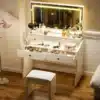 Tualettlaud LED valgustusega ja viie sahtliga | E-pood Tootemaailm Elegantne valge tualettlaud LED valgustusega ja viie suure mahuka sahtliga, peegel erinevate kosmeetikatoodetega, puidust põrand ja valgusküllane taust.