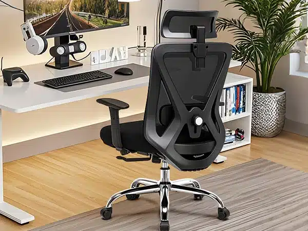 Must ergonoomiline kontoritool, millel on 3D peatugi ja nimmetugi, paikneb kaasaegses kontoriruumis valge kirjutuslaua ees, tooli metallist jalgadel on rattad.
