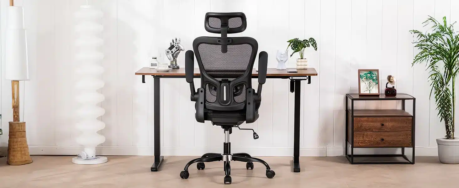 Kontoritool ergonoomiline võrkpehmendus reguleeritava peatoega, musta värvi võrkmaterjalil ja liikuvate ratastega, asetseb kodukontoris puidust laua taga, valge seina ja taimede taustal.
