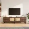 TV-alus tume puit rattanustega, 180 cm, 4 sahtlit | E-pood Tootemaailm Elutoas asuv TV-alus tume puit rattanustega, 180 cm lai ja nelja sahtliga, asetatud heledale puidust põrandale valgusküllasel taustal, kus paremal on näha roheline taim.