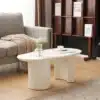 Kohvilaud valge MDF-ga, 100 cm, kaarja disainiga | E-pood Tootemaailm Kaunis valge MDF pinnaga kohvilaud, millel on elegantne kaarjas disain. Laud on asetatud elutoas heleda parketiga põrandale, kõrval hall diivan ja raamaturiiul seinal.