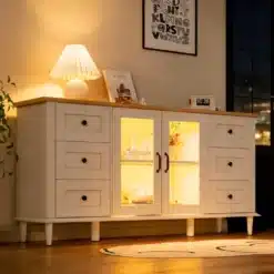 Elegantselt valgustatud kummut LED valgustusega, kuue sahtli ja klaasustega, mis seisab puidust põrandal. Kummuti pealne on dekoreeritud lampide ja raamatutega ning taustal on seinal maal.