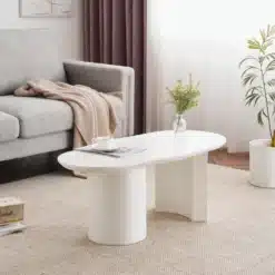 Valge MDF-st kaarja disainiga kohvilaud, 100 cm, paigutatuna stiilsesse elutuppa, mille taustal on hall diivan ja lillad kardinad.