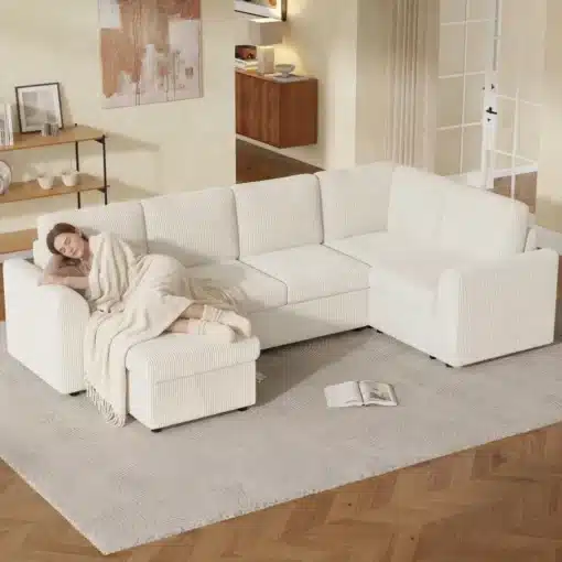 Nurgadiivan sametist käetugedega ja tumba | E-pood Tootemaailm Elegantne valge nurgadiivan sametist käetugedega, millel lamab naine pehme pleedi all. Diivan asub avaras elutoas helepruunil vaibal, luues sooja ja kutsuva atmosfääri.