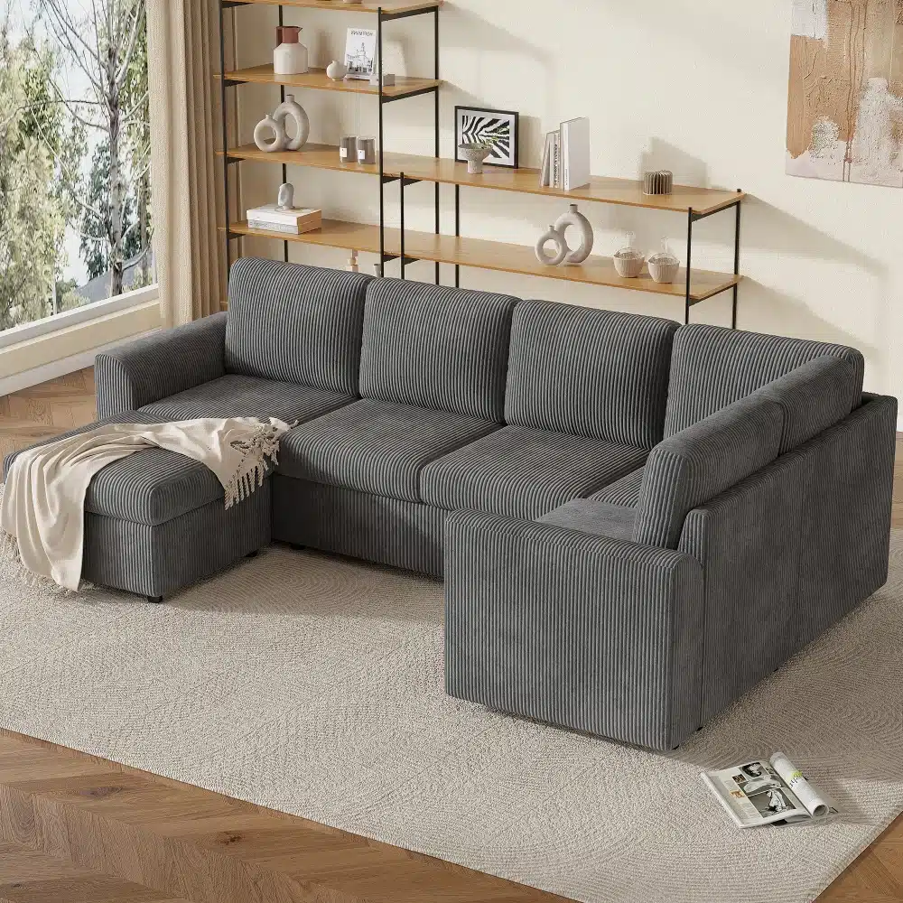 Elegantne hall nurgadiivan sametist käetugedega ja tumba, sobib kaasaegsesse elutuppa, vaipkattega põrandal ja puidust riiuli ees.