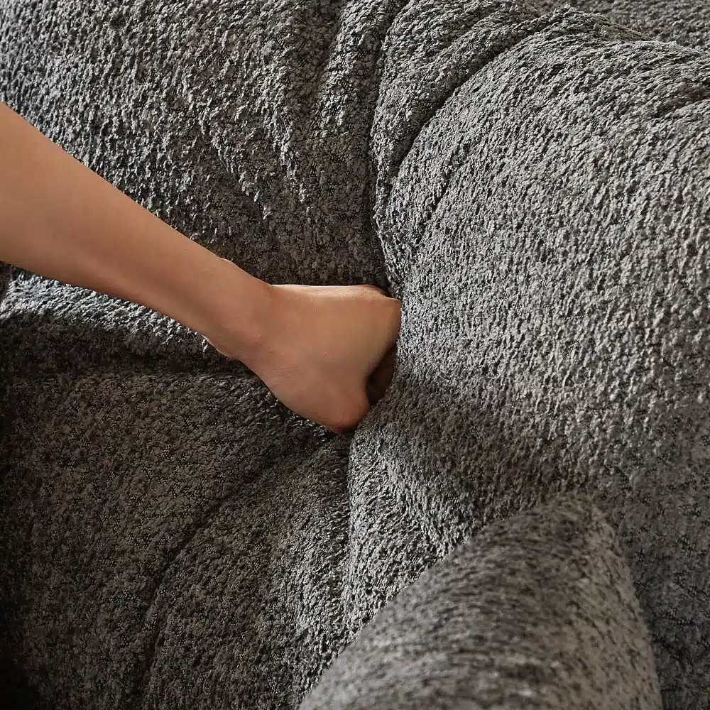 Käsi surub halli chenille kangast nurgadiivani polstrit, näidates materjali pehmust ja elastsust.