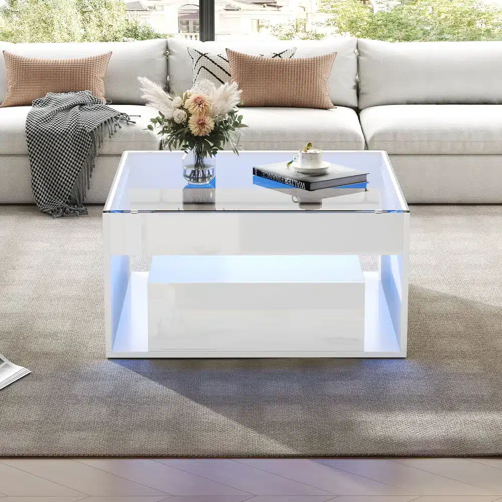 Diivanilaud LED-valgustusega ja kahe sahtliga modernses elutoas. Valge läikiva pinnaga laud, millel on läbipaistev klaaspind. Laua all helendavad sinised LED-tuled ja taustaks on hele diivan.