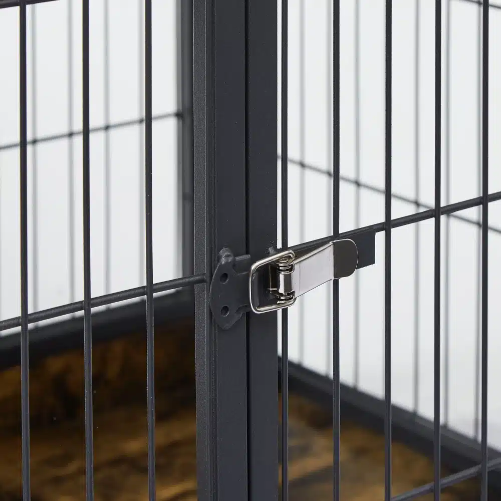 Lähivõte koerakuudi kahekordsete ustega metallist lukustusmehhanismist, mis tagab turvalisuse ja vastupidavuse. Puidust detailid taustal annavad kuudile hubase välimuse.