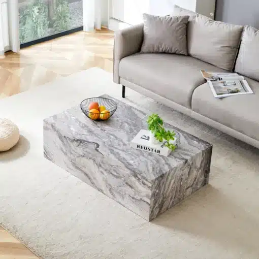 Kohvilaud marmoriefektiga MDF hall 90×50×30 cm nordic stiil | E-pood Tootemaailm Marmoriefektiga MDF hall kohvilaud nordic stiilis, asetatud heledale vaibale avaras elutoas, diivani ees. Laual on musta traadist puuviljakorv ja roheline taim. Valgusküllase toaga taust rõhutab laua elegantset disaini.
