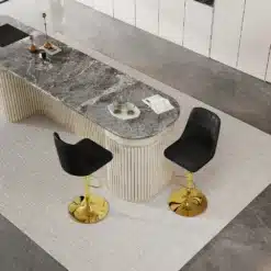 Pildil on kaks modernset baaritooli, millel on reguleeritava kõrgusega kuldsed jalad ja mustad seljatoed. Toolid asetsevad elegantse, heledast kivist köögisaare kõrval, hallil põrandal vaibal.