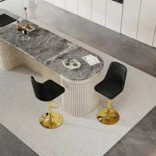 Pildil on kaks modernset baaritooli, millel on reguleeritava kõrgusega kuldsed jalad ja mustad seljatoed. Toolid asetsevad elegantse, heledast kivist köögisaare kõrval, hallil põrandal vaibal.