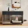 Puidust kassiliivakasti kapp integreeritud toidukausiga, mille sees on hall kass. Kapp on vintage stiilis, looduslike puidumustritega ja musta pealsega. Taustal on hele sein, millel on minimalistlik kunst ja vaas rohelise oksaga.
