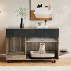 Puidust kassiliivakasti kapp integreeritud toidukausiga, mille sees on hall kass. Kapp on vintage stiilis, looduslike puidumustritega ja musta pealsega. Taustal on hele sein, millel on minimalistlik kunst ja vaas rohelise oksaga.