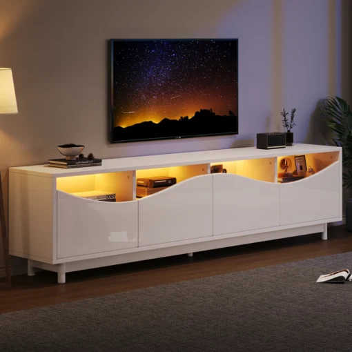 TV-alus LED-valgustusega, valge kõrgläige, 175 cm | E-pood Tootemaailm Valge kõrgläikega TV-alus LED-valgustusega, mõõtmetega 175 cm, modernses elutoas tumedal puidust põrandal. Alus sisaldab mitut riiulit, millel on kollane valgustus, ning sellel on asetatud dekoratiivsed esemed, taustal on lamp ja televiisor.