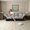 Diivanvoodi 3-in-1, samet, queen-size, 190 cm, | E-pood Tootemaailm Diivanvoodi 3-in-1, samet, queen-size, 190 cm, kauni halli värviga, asub modernses elutoas beeži vaiba peal. Naine istub diivanil, hoides käes puldi ja kohvitassi.