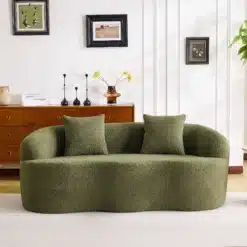 Kahekohaline kumer diivan kahe padjaga elutuppa, oliivroheline pehme kangas, minimalistlik disain, hele sein ja puitmööbel taustal.