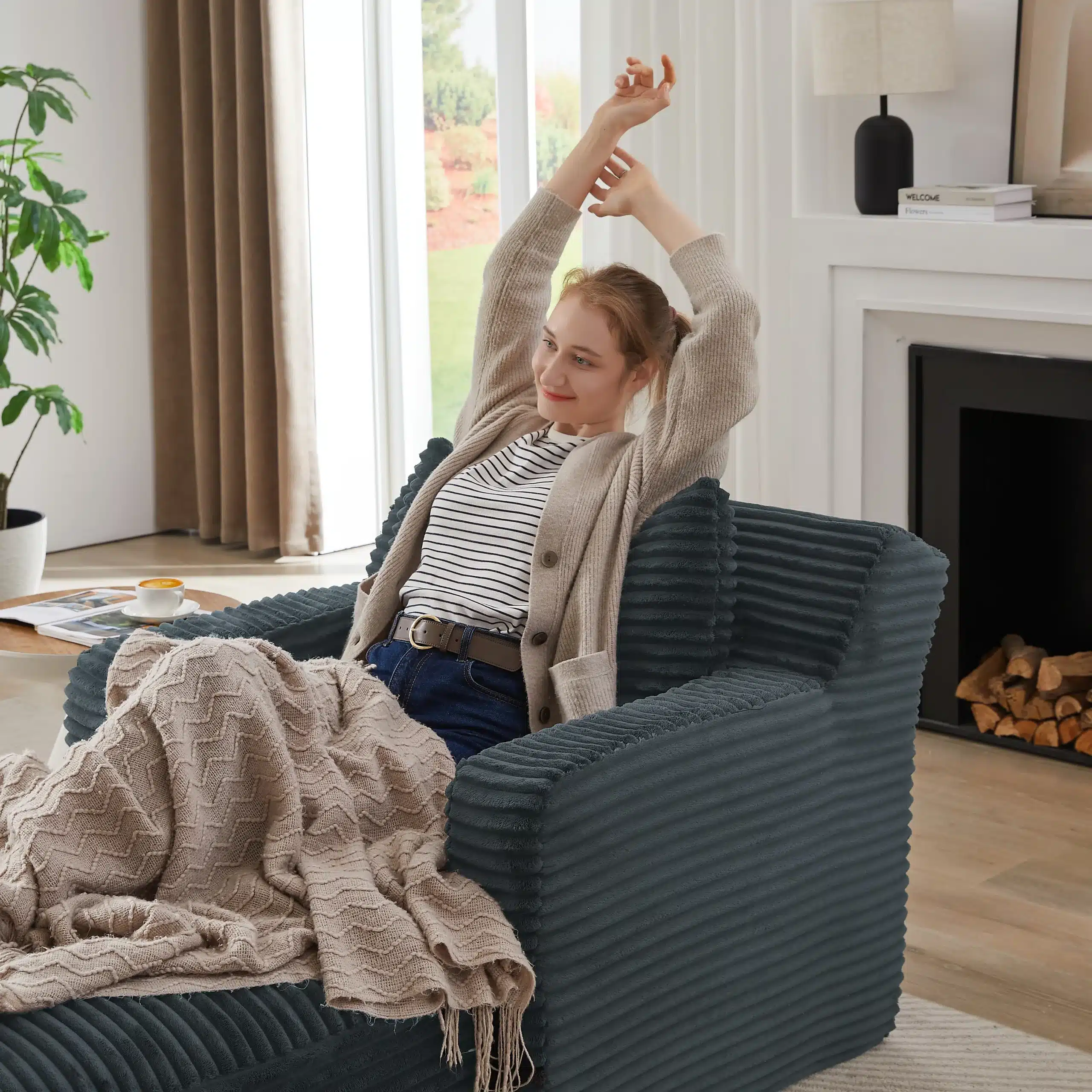 Naeratav naine lõõgastub Super mugav ja kvaliteetne diivanivoodil, millel on pehme tumehall kangas ja silmapaistvad triibulised padjad. Diivan asub heledas ja modernses elutoas koos kaminaga, mille kõrval kasvab roheline toataim.