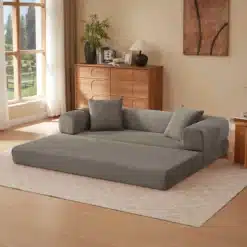 Kokkupandav sametist diivanvoodi, khaki värvi ja pehme, beige vaiba peal hubases elutoas puidust mööbliga, akende ja taimede kõrval.