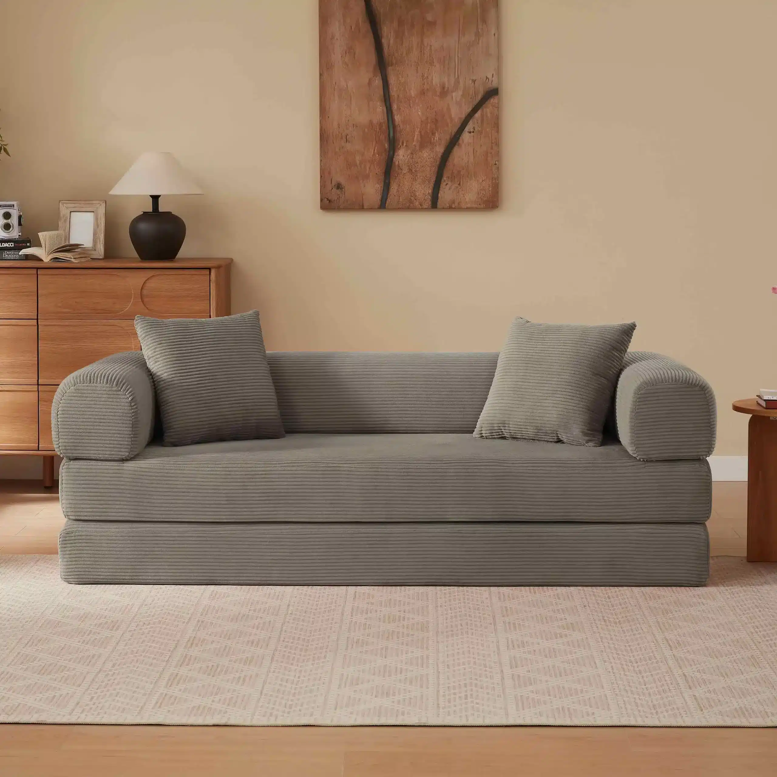 Elegantne kokkupandav diivanvoodi, mis on kaetud pehme khaki värvi sametiga, asetatud sooja tooniga elutuppa, kus on puidust mööbel ja mahedad dekoratsioonid.
