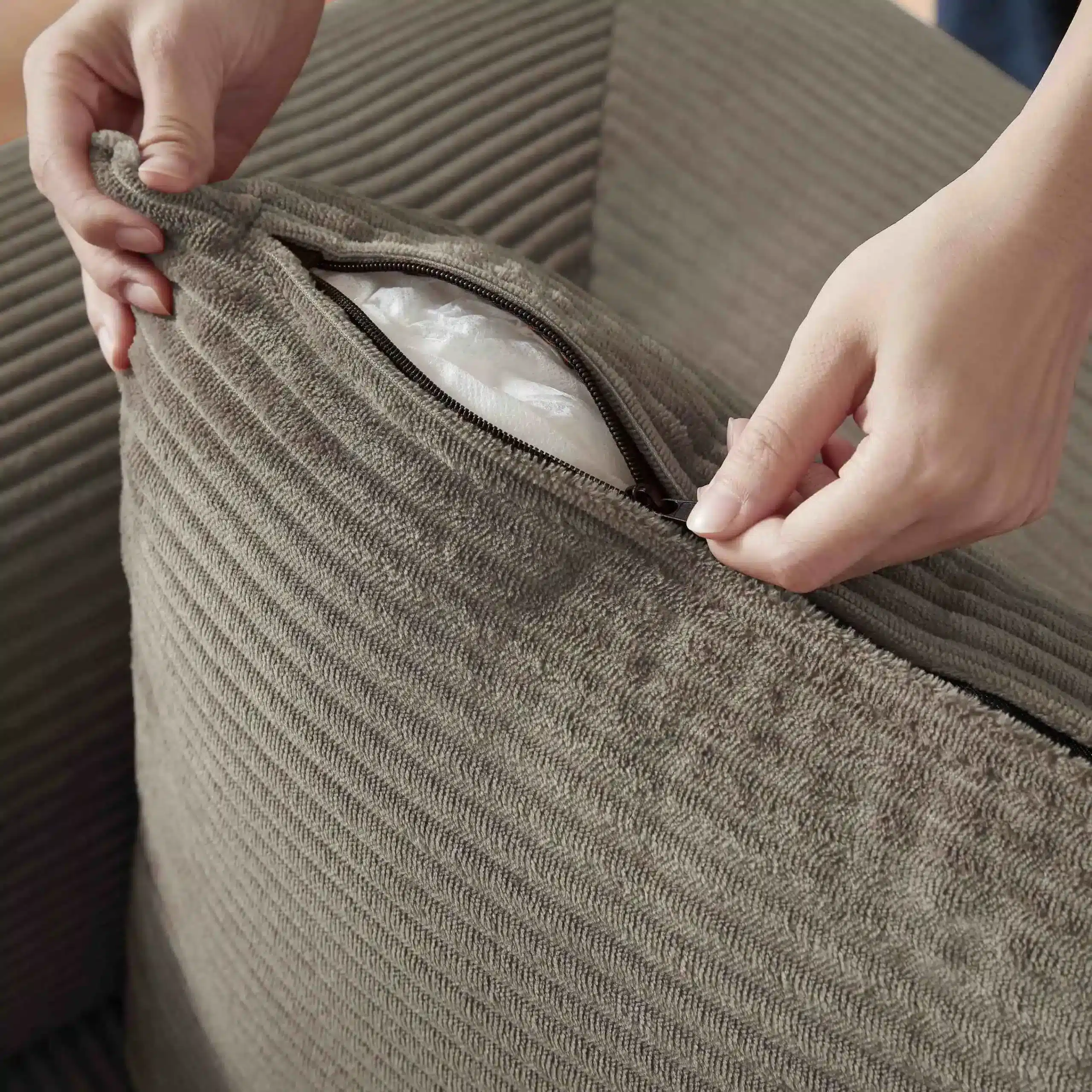 Käed avavad khaki värvi sametist diivanvoodi padja tõmblukuga taskut, paljastades pehme täidise taustal, mis lisab mugavust ja praktilisust.