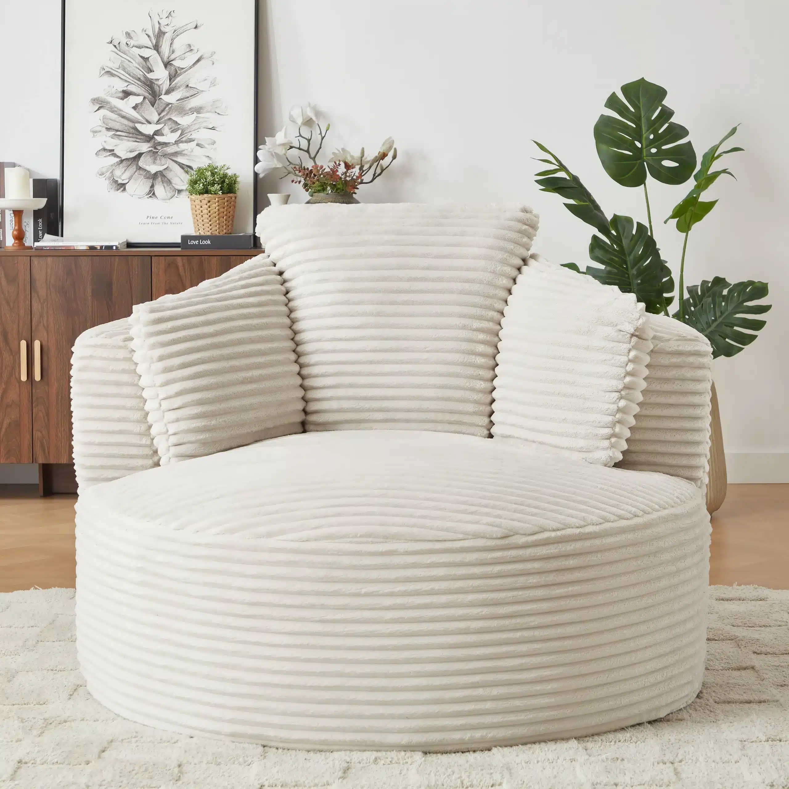 Ümar tugitool elutuppa, magamistuppa või lastetuppa, mis on kaetud pehme kreemivärvi kangaga, asetatud beežile vaibale modernses elutoas, mille taustal on tumepuidust kapp ja rohelised toataimed.