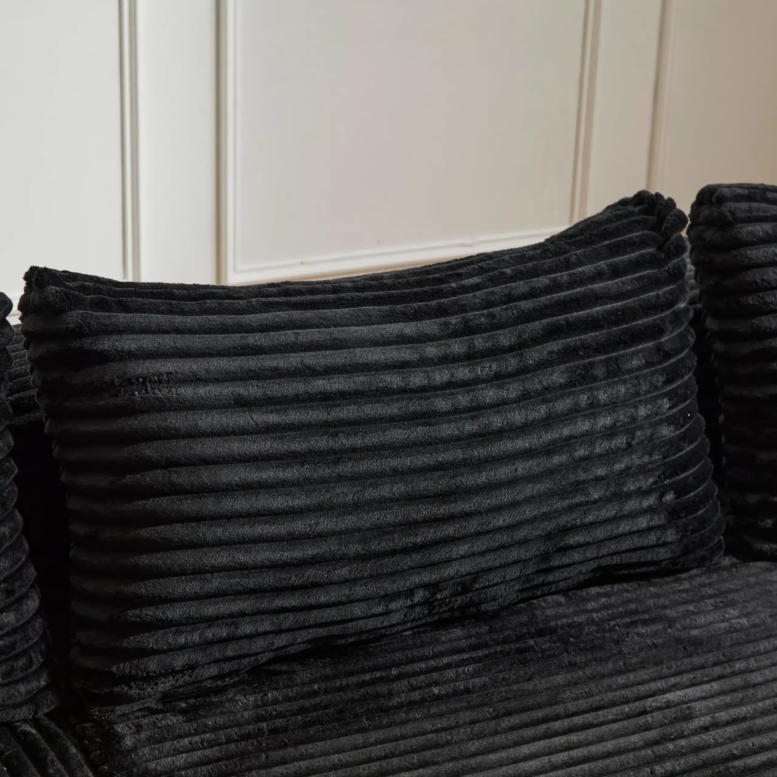 Musta värvi väga mugava muuduldiivani pehme padi, ribilise tekstuuriga ja elegantselt asetatud puhtale taustale.